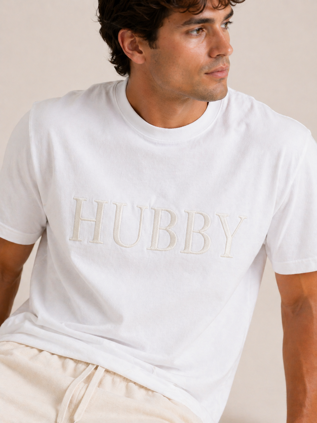 Man wearing a white t-shirt with 'HUBBY' printed on it against a beige background