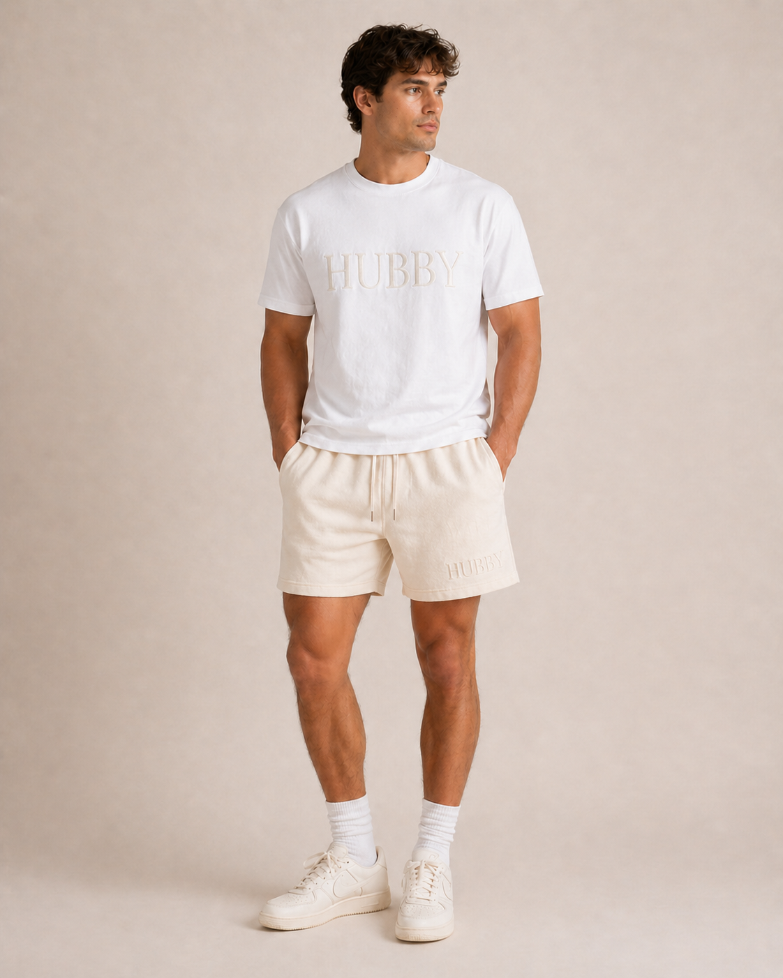 Man wearing a white 'HUBBY' t-shirt and beige shorts on a plain background